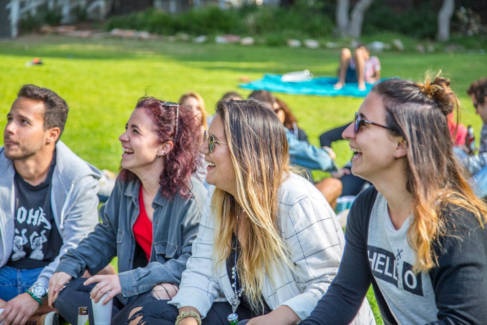 grupo de amigos mirando de perfil a cámara y sonriendo. Están sentados en el césped 